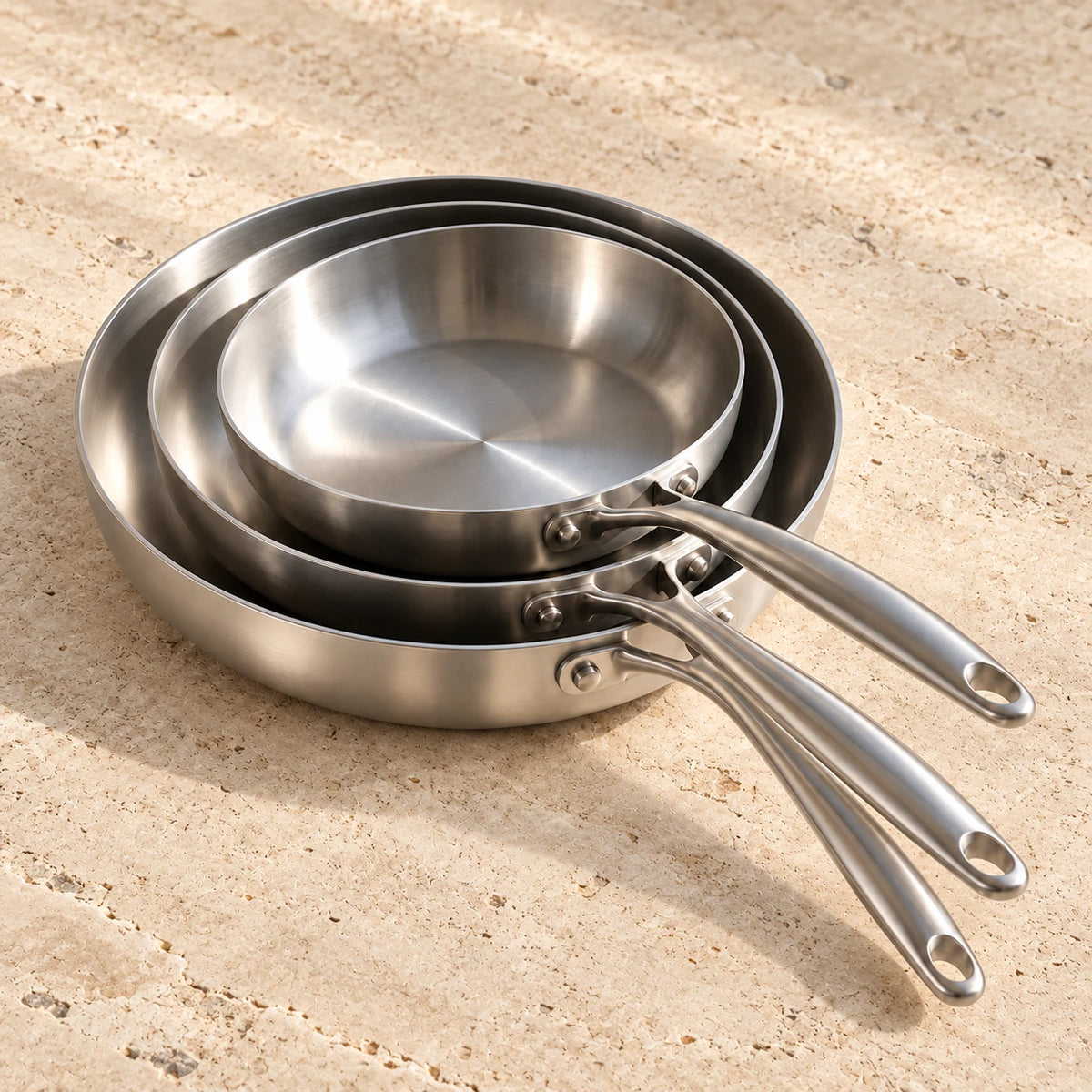Pack Apprenti LAEVOR : les trois poêles inox 316 sur un plan de travail en travertin